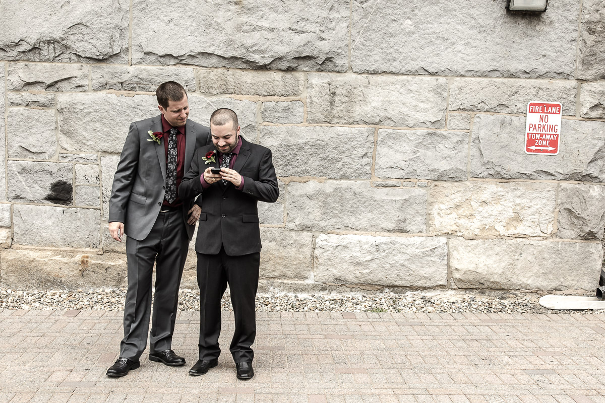 Contact wedding photographer for candid moments like this—two groomsmen reading a phone together during a Boston wedding.