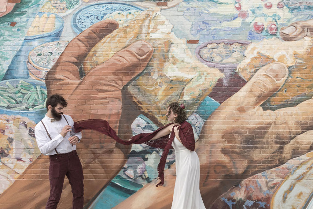 Spagnolo Photography captures a creative, non-traditional wedding moment with a couple and red scarf in front of a vibrant mural in Cambridge, by the best wedding and couples photographer