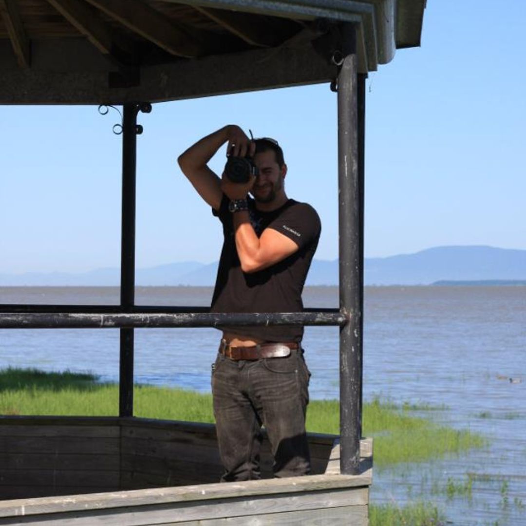 Aaron Spagnolo photographing a marshy coastline from a balcony.