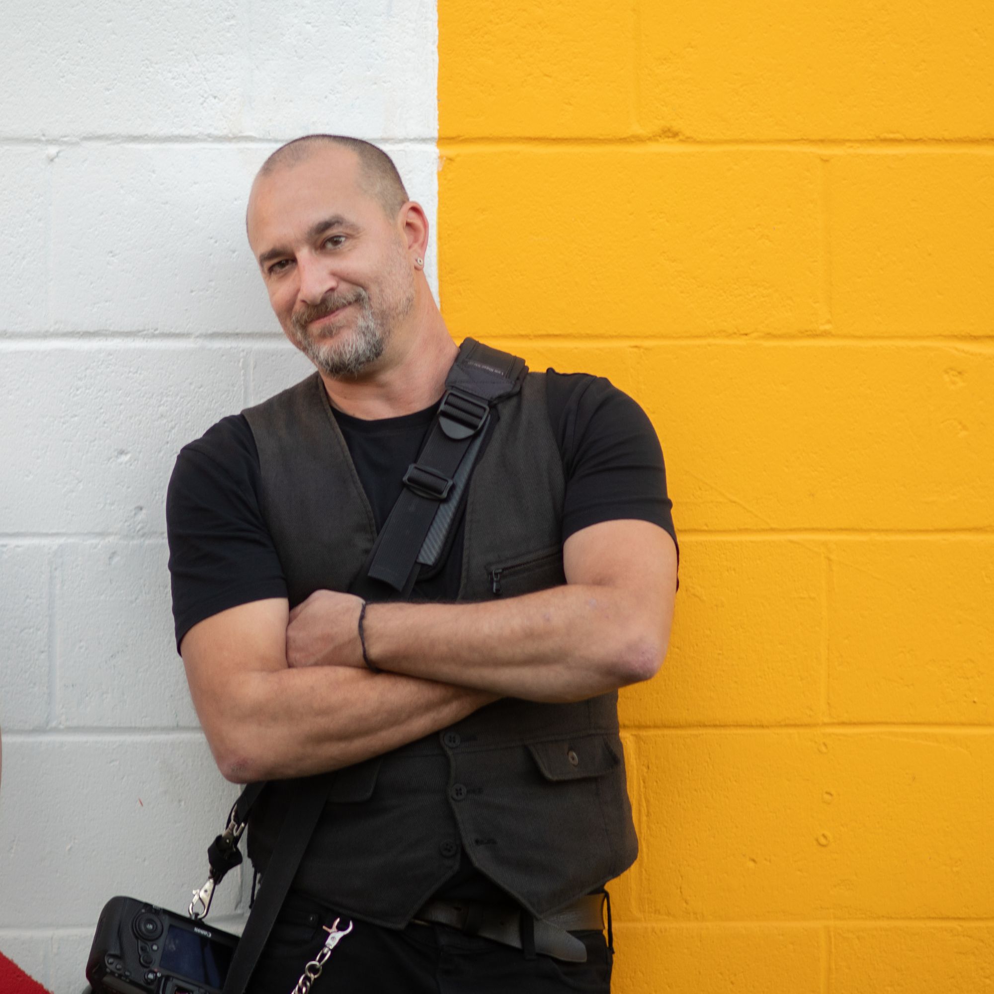Boston wedding photographer Aaron Spagnolo leans against a yellow wall.