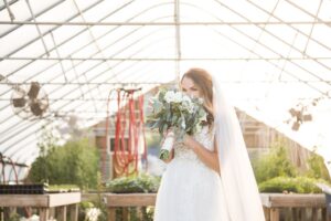 A bride smells her flowers in the greenhouse of the Barn at Gibbet Hill in Groton, MA on her wedding day - image featured along with the bride's glowing review of her wedding photographer Spagnolo Photography.