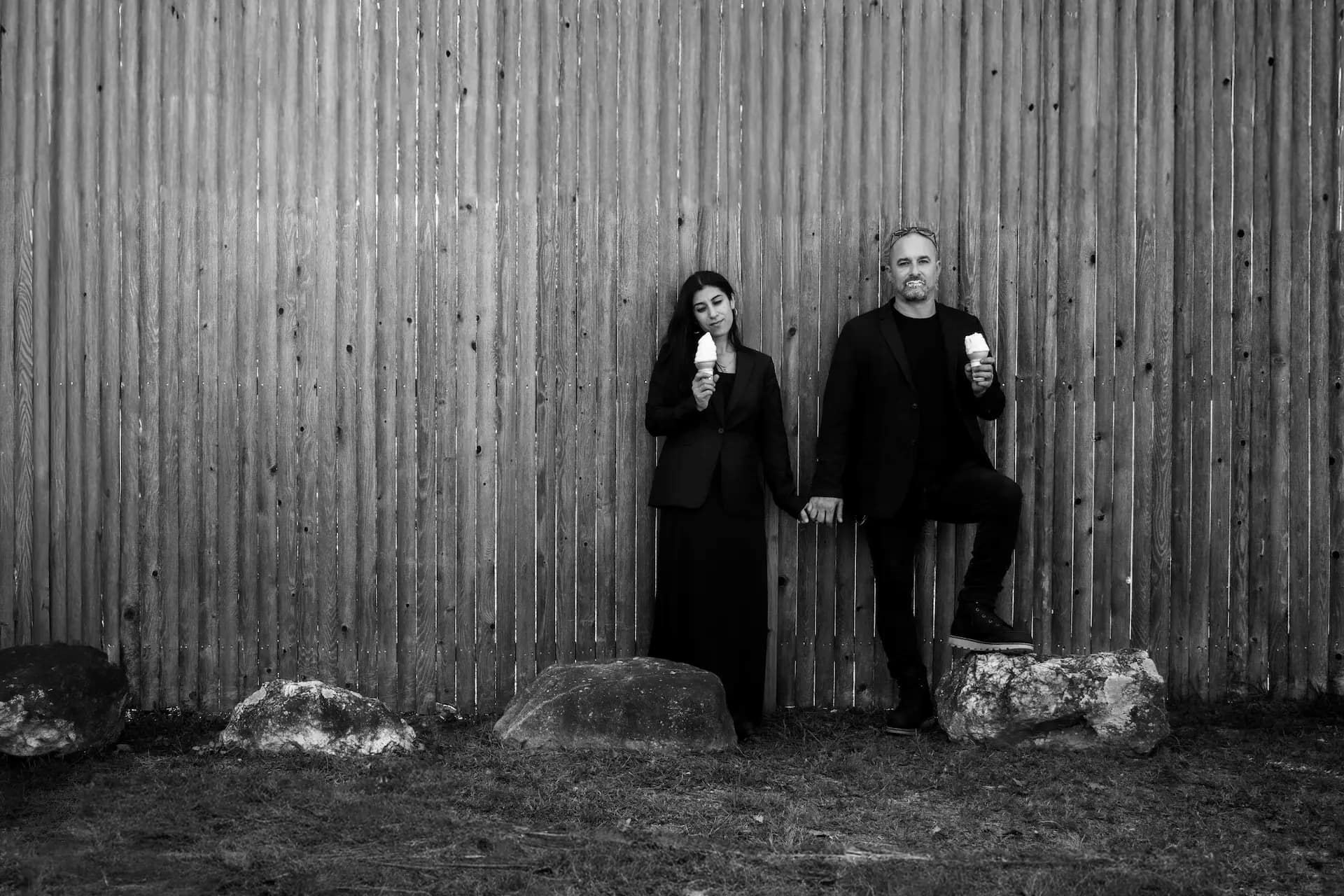 A black and white image of Boston wedding photographers Aaron and Nanore of Spagnolo Photography leaning against a fence and eating ice cream.