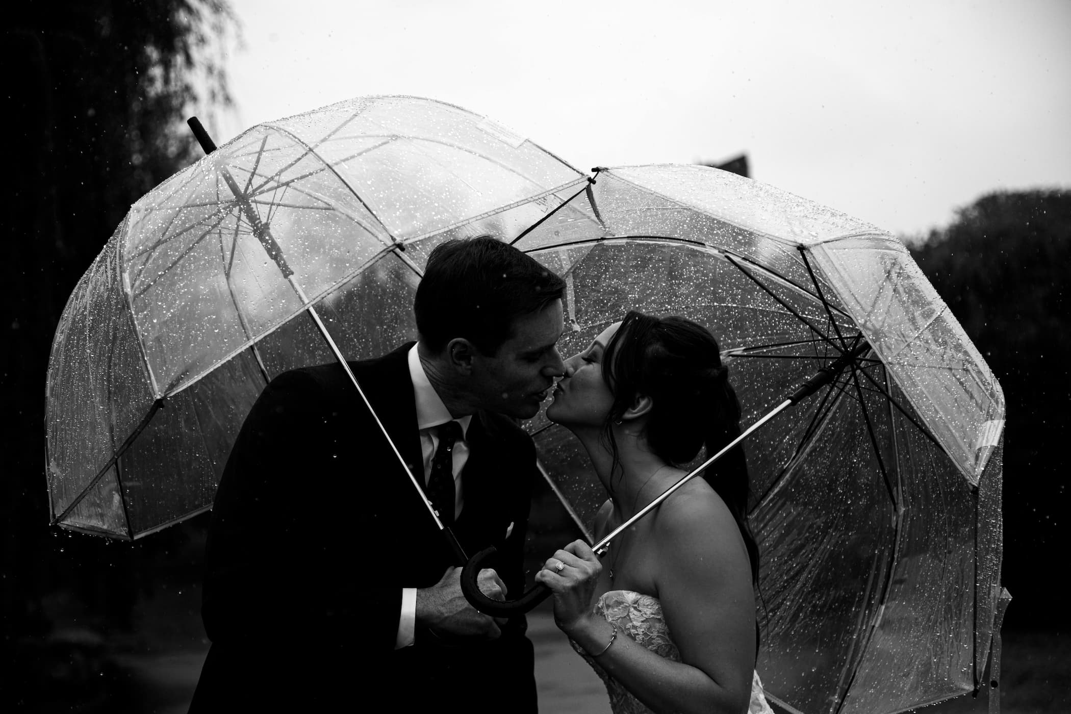 A romantic black and white Boston Wedding portrait of a bride and a groom kissing under their umbrellas during their first look on the Boston Common, photographed by Boston wedding photographers Spagnolo Photography