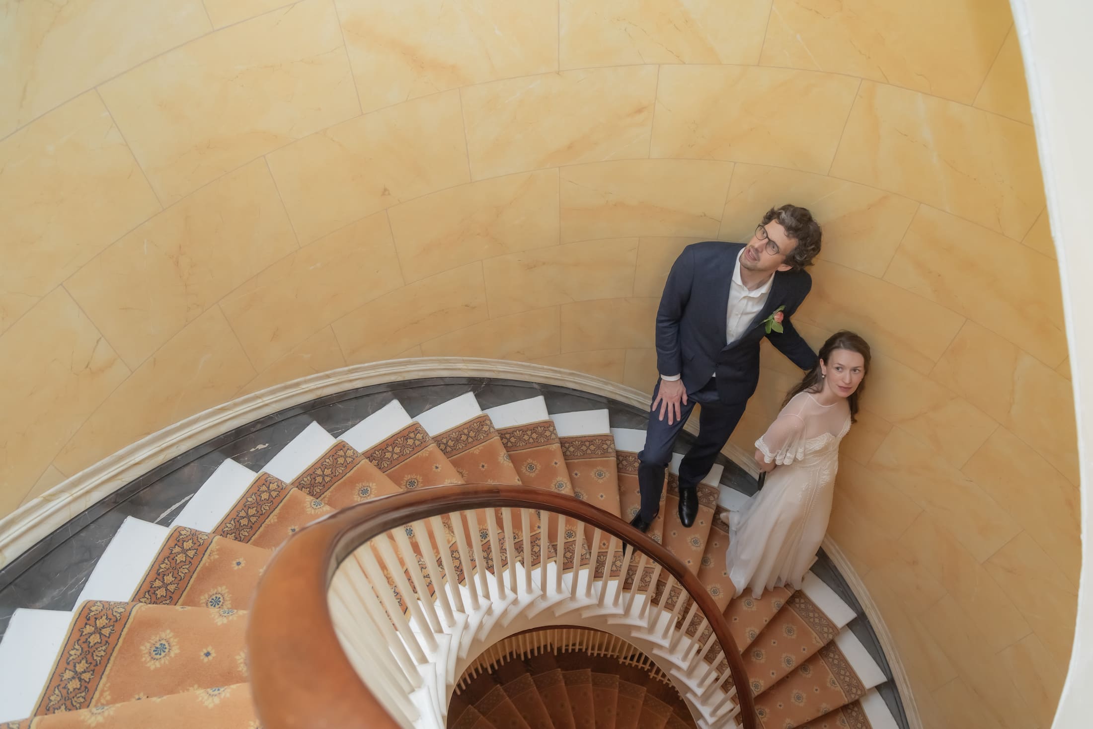 A bride and groom stand on a spiral staircase with a yellow wall at their Beacon Hill brownstone micro-wedding, photographed by Spagnolo photography