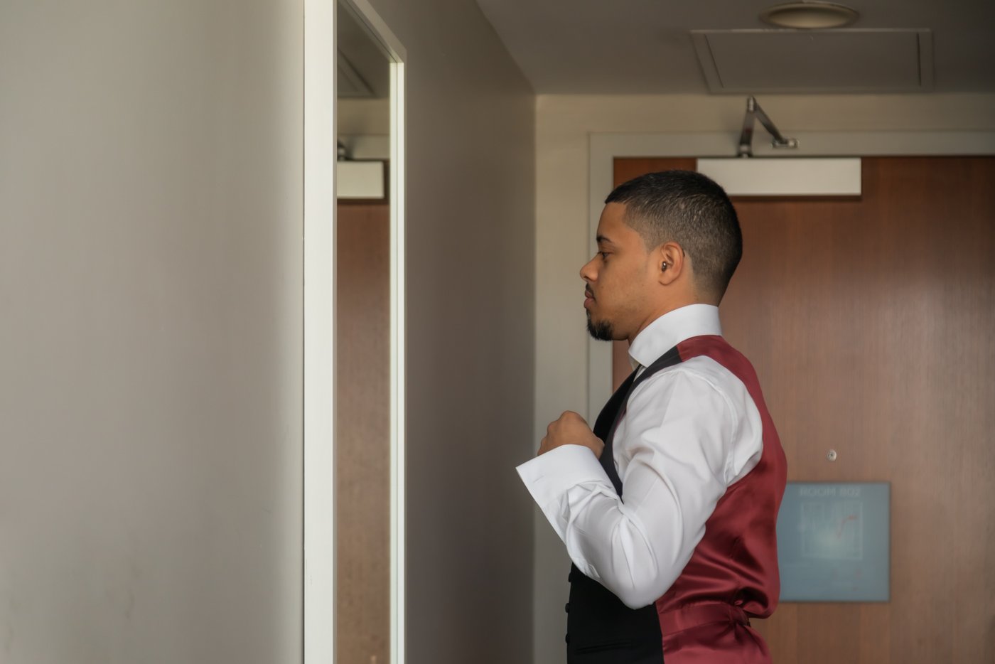 Groom adjusting his shirt while looking in the mirror at The Godfrey Hotel in Boston