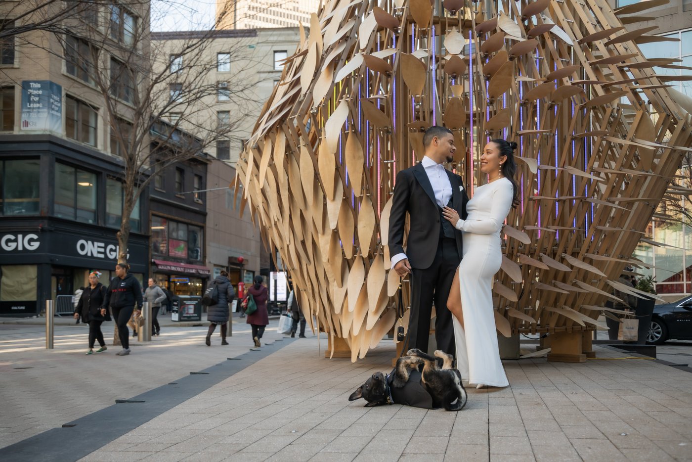Bride and groom pose and smile at each other by a sculpture on their way to elope at Boston City Hall