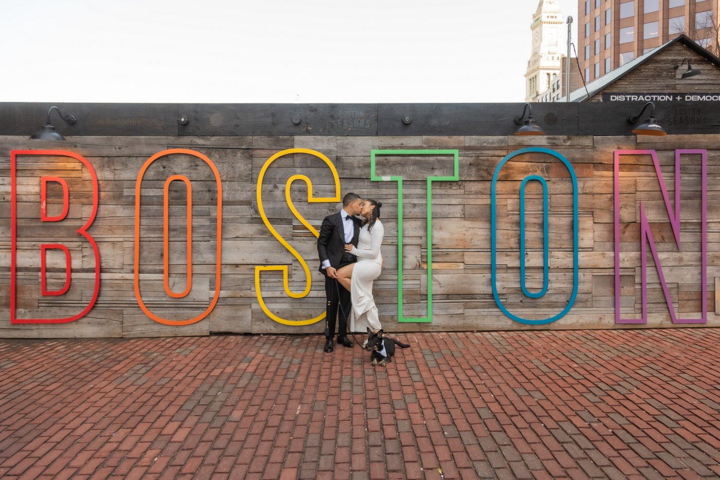 Bride and groom kissing by the multicolor "BOSTON" sign on their way to elope at Boston City Hall