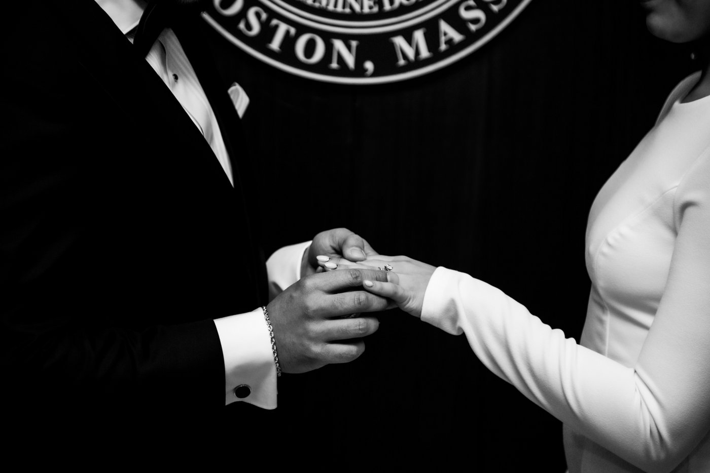 A black and white close up image of the groom sliding the wedding ring on the bride's finger during their Boston City Hall wedding ceremony.