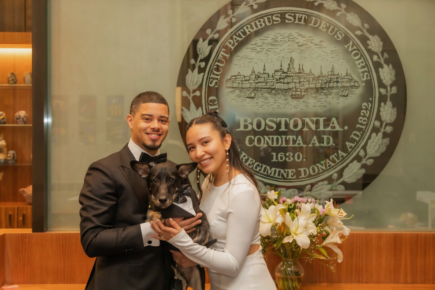 The bride and groom and their dog posing by the Boston seal at Boston City Hall on their wedding day