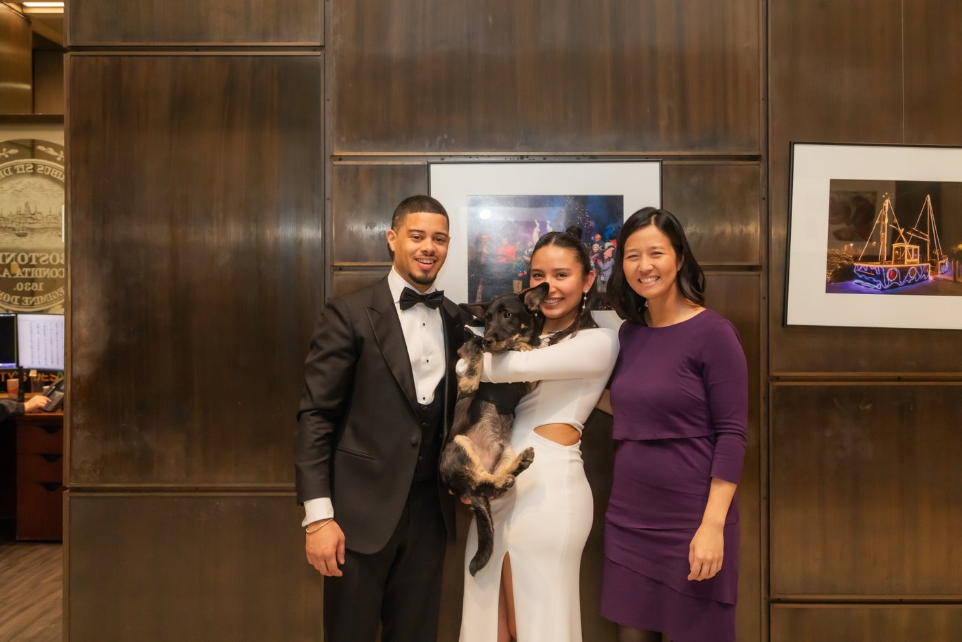 A portrait of Boston Mayor Michelle Wu posing with a newlywed couple and their dog in a tuxedo who served as witness during a Boston City Hall wedding elopement ceremony