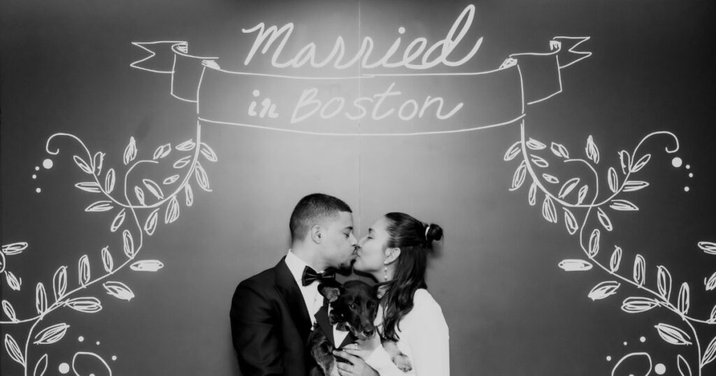 Boston City Hall wedding photographers Spagnolo Photography capturing a black and white image of a bride and a groom kissing under the "Married in Boston" sign following their Boston City Hall elopement.