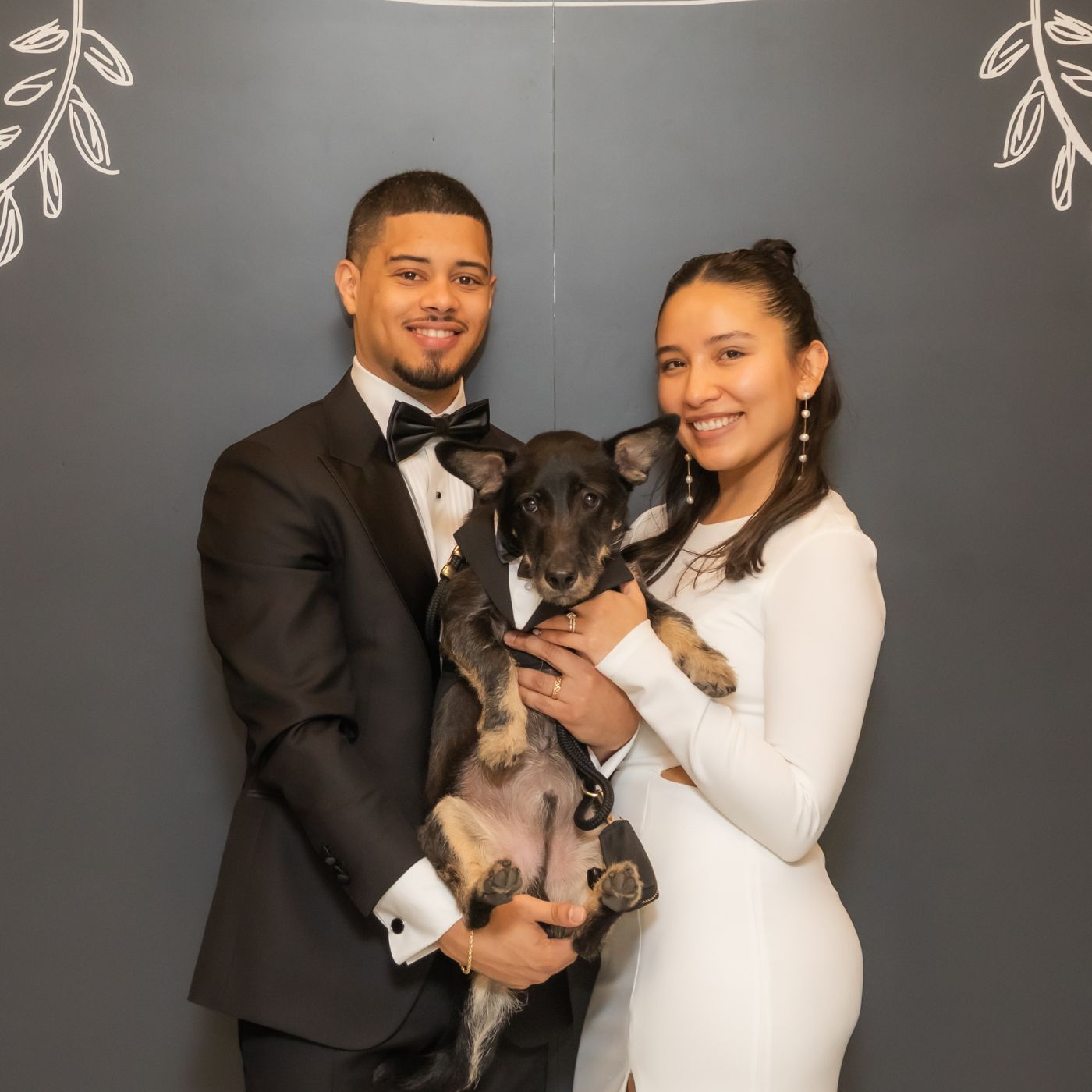 A cute little dog dressed in a tuxedo poses for a portrait with his owners, after serving as witness at their Boston City Hall wedding, where dogs are allowed to become marriage witnesses
