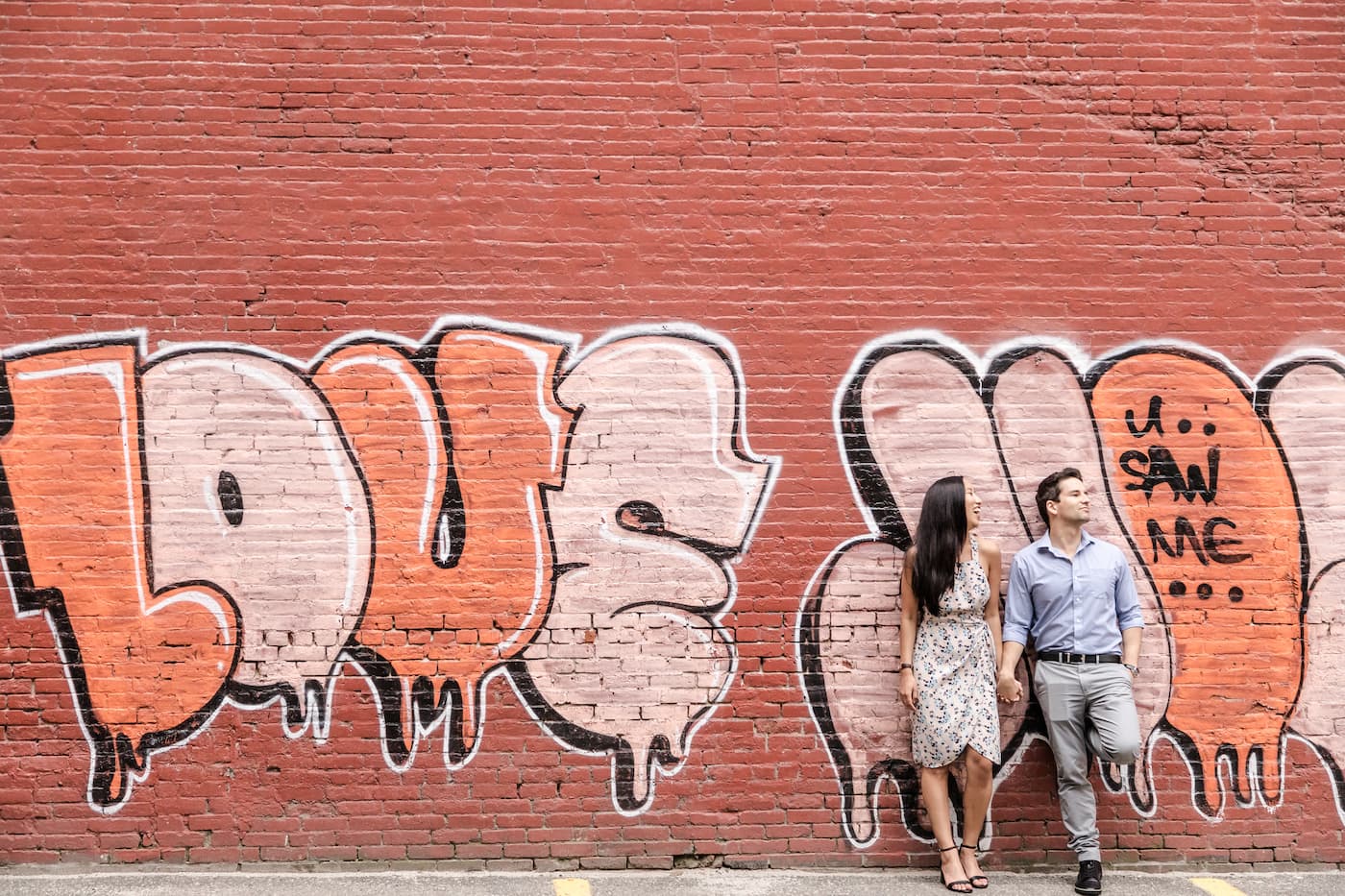 During a couples photography session with Boston engagement photographers Spagnolo Photography, a couple leans against a red wall, next to a graffiti that reads "love" in bubble letters