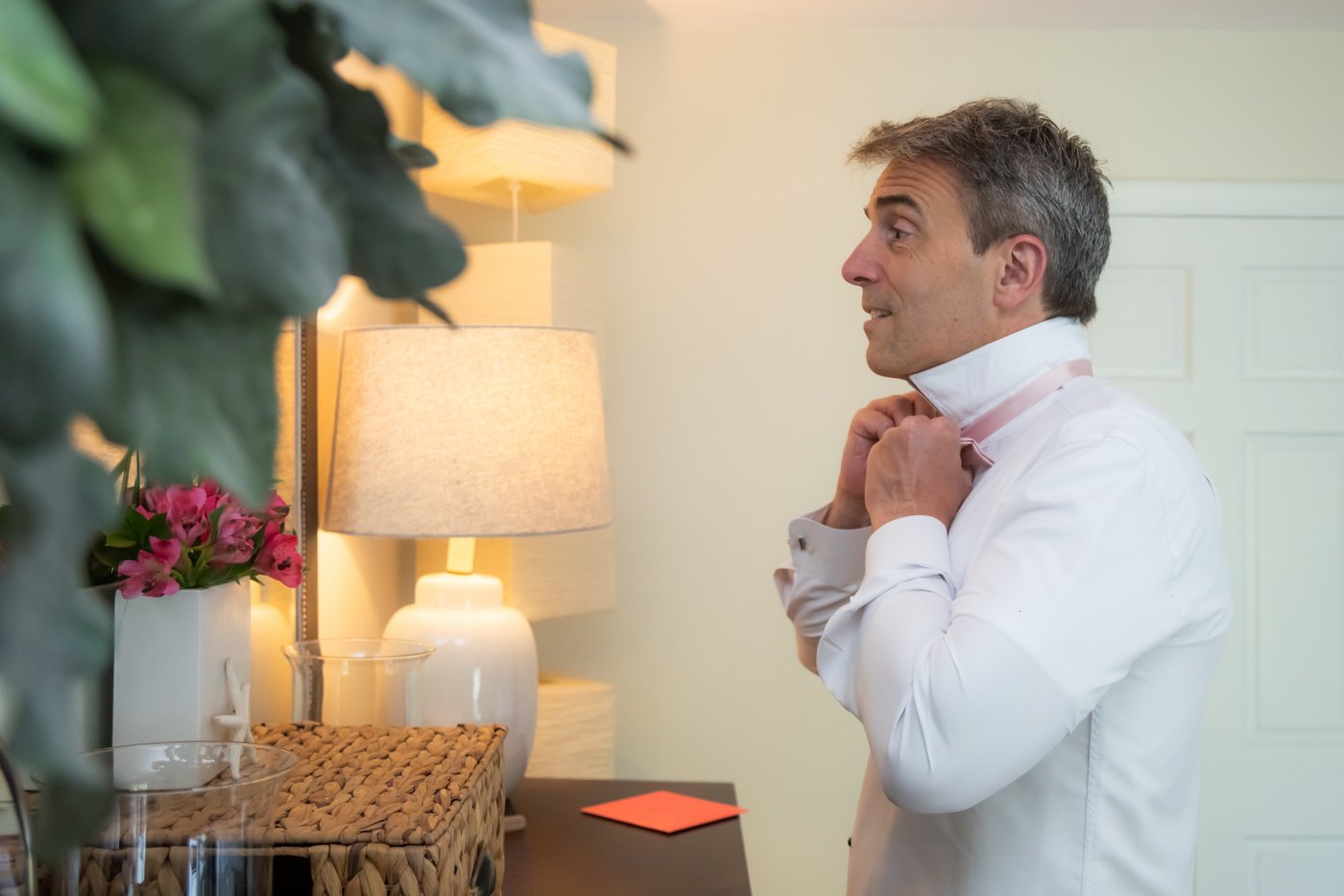 A side shot of the groom fixing his bowtie.
