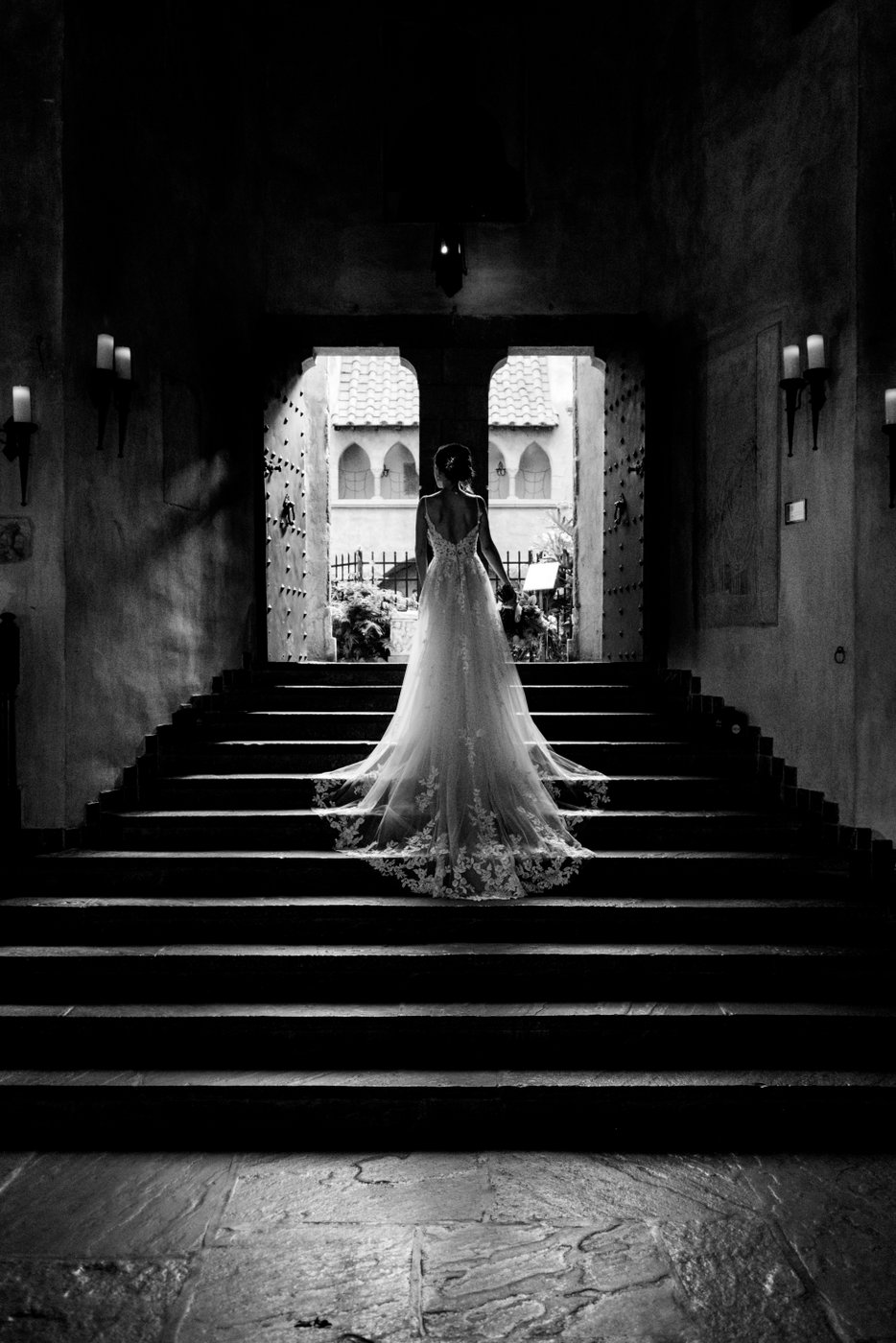 A black and white photo of the bride on the Great Hall stairs at Hammond Castle, the train of her dress cascading down the stairs, minutes before the start of her wedding ceremony.