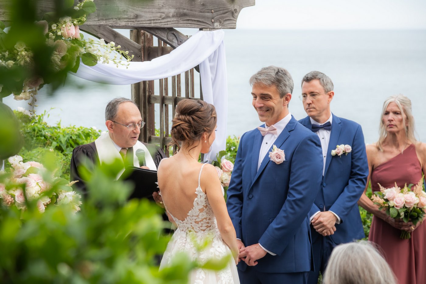 The groom smiles at the bride during their summer Hammond Castle wedding ceremony overlooking the ocean in Gloucester