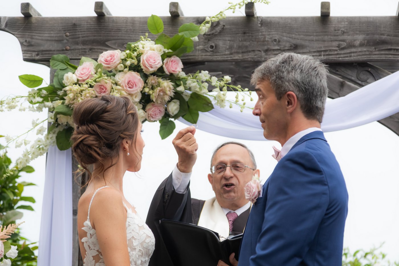 The officiant holds up a wedding band as the bride and groom listen to his words during a Hammond Castle wedding ceremony