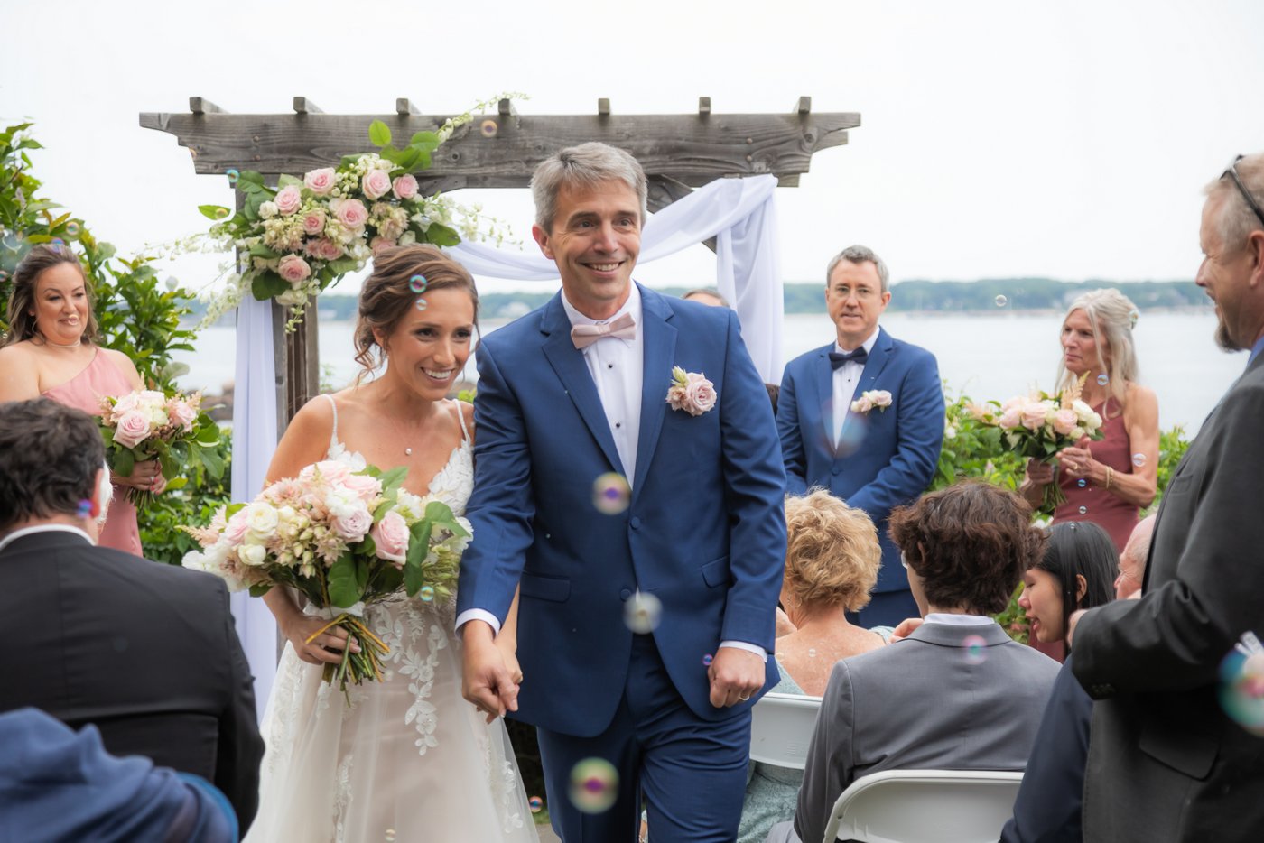 The bride and groom walk up the aisle at the end of their Hammond Castle wedding ceremony as guests blow bubbles