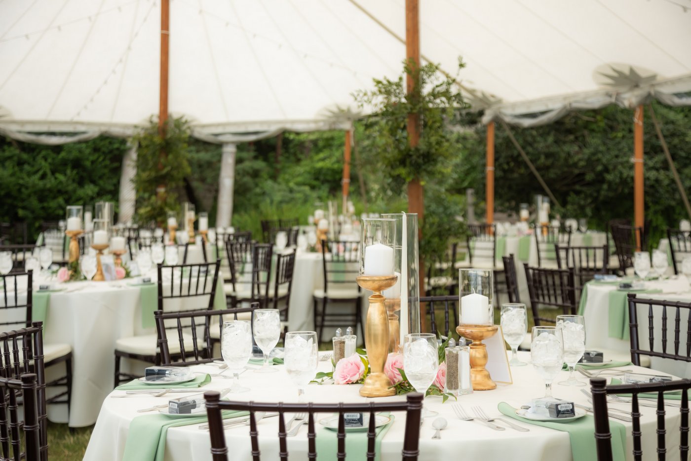 The table settings, gold candle holders, and pink roses in the wedding reception tent at Hammond Castle