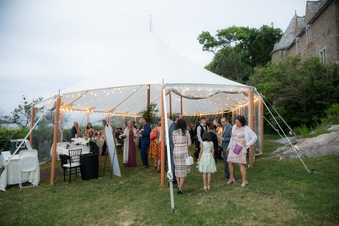The string lights glow in the wedding reception tent on the oceanside lawn of Hammond Castle Museum