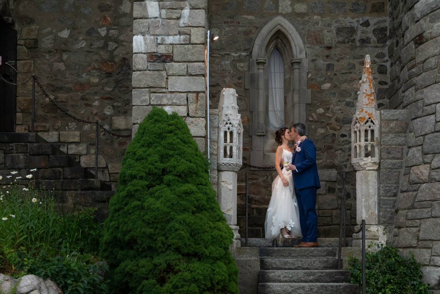 The bride and groom kiss on the stone steps behind Hammond Castle, overlooking their wedding ceremony space.