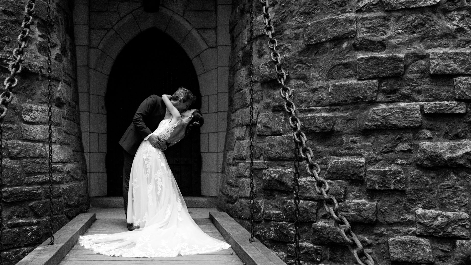A black and white photo of the groom dipping and kissing the bride on the Hammond Castle drawbridge, before the wedding reception