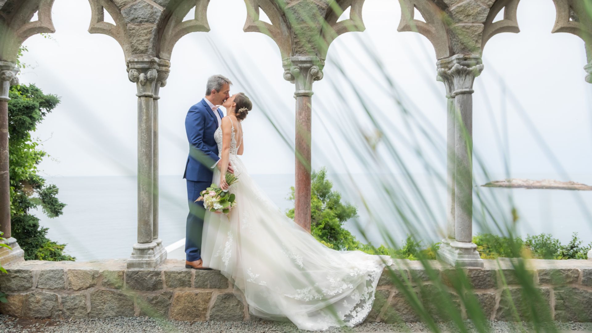 A bride and a groom kiss by the stone arches during their Hammond Castle Museum wedding in Gloucester.