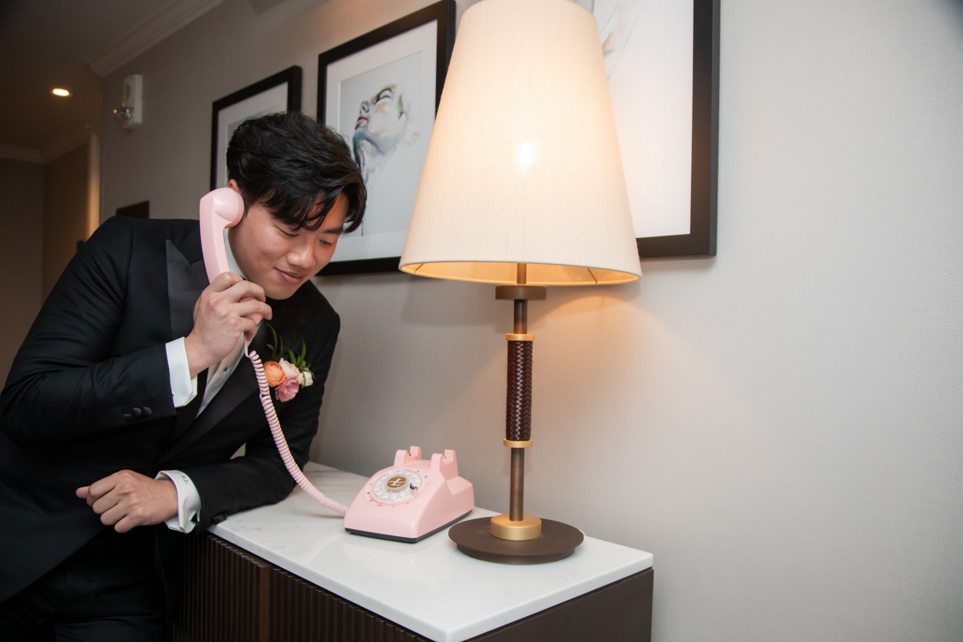 Groom holding the receiver of a vintage pink phone to his ear at the Langham Hotel in Boston
