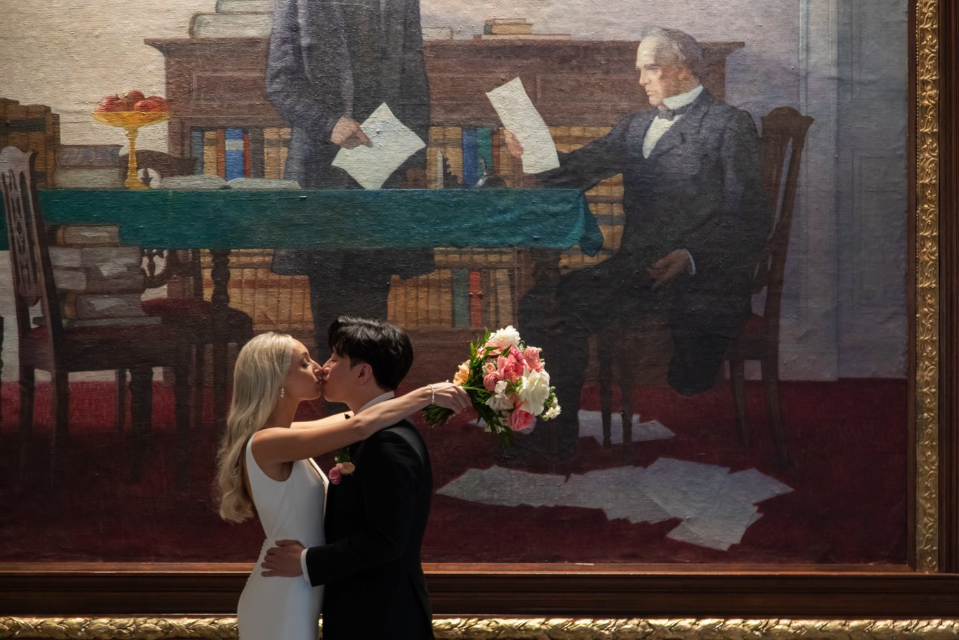 The bride and groom kiss before a historic painting in the Wyeth Room in Boston's Langham Hotel