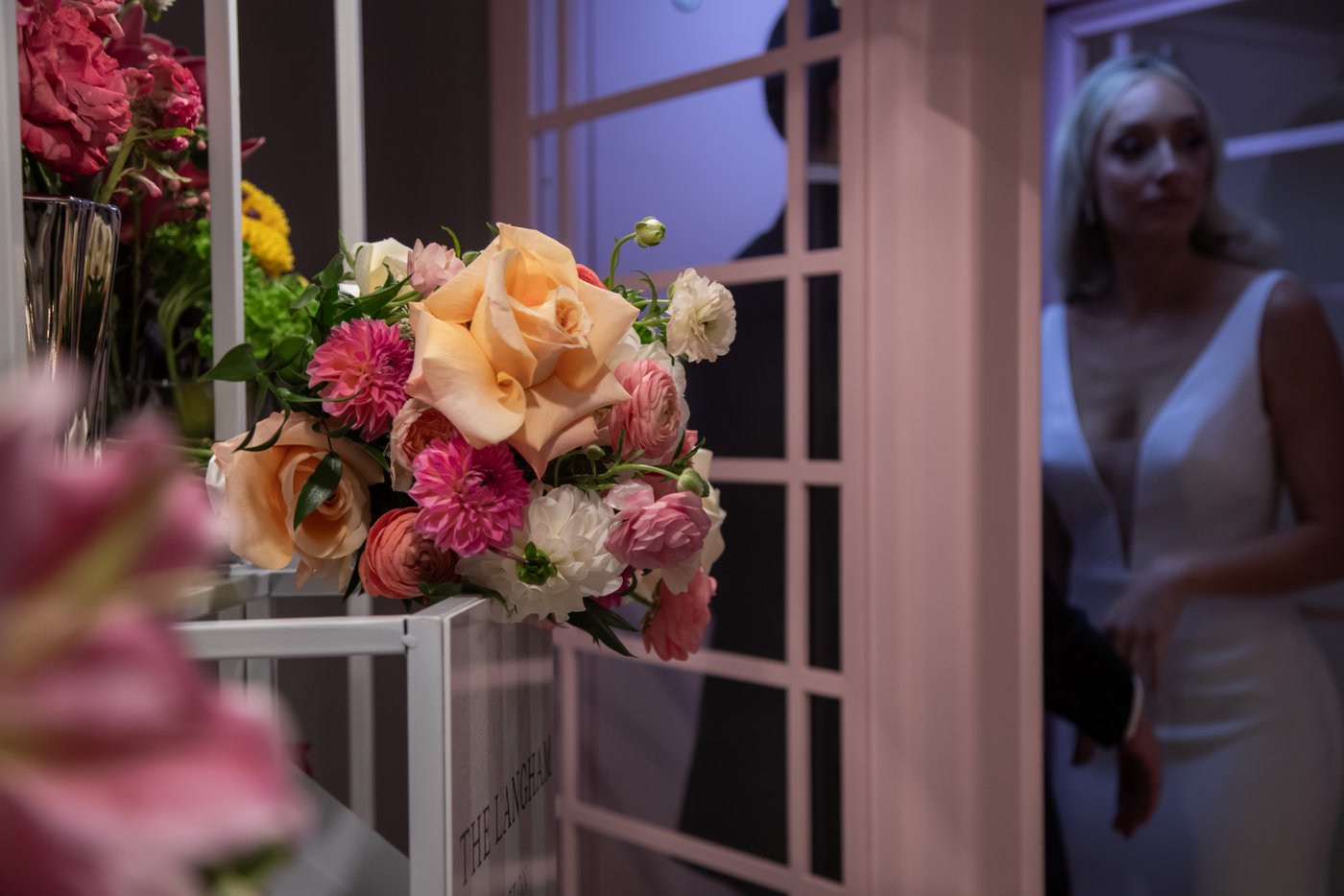 A candid, artistic, and moody shot of the bride and groom on their wedding day exiting the Langham Hotel Boston's iconic pink phone booth.