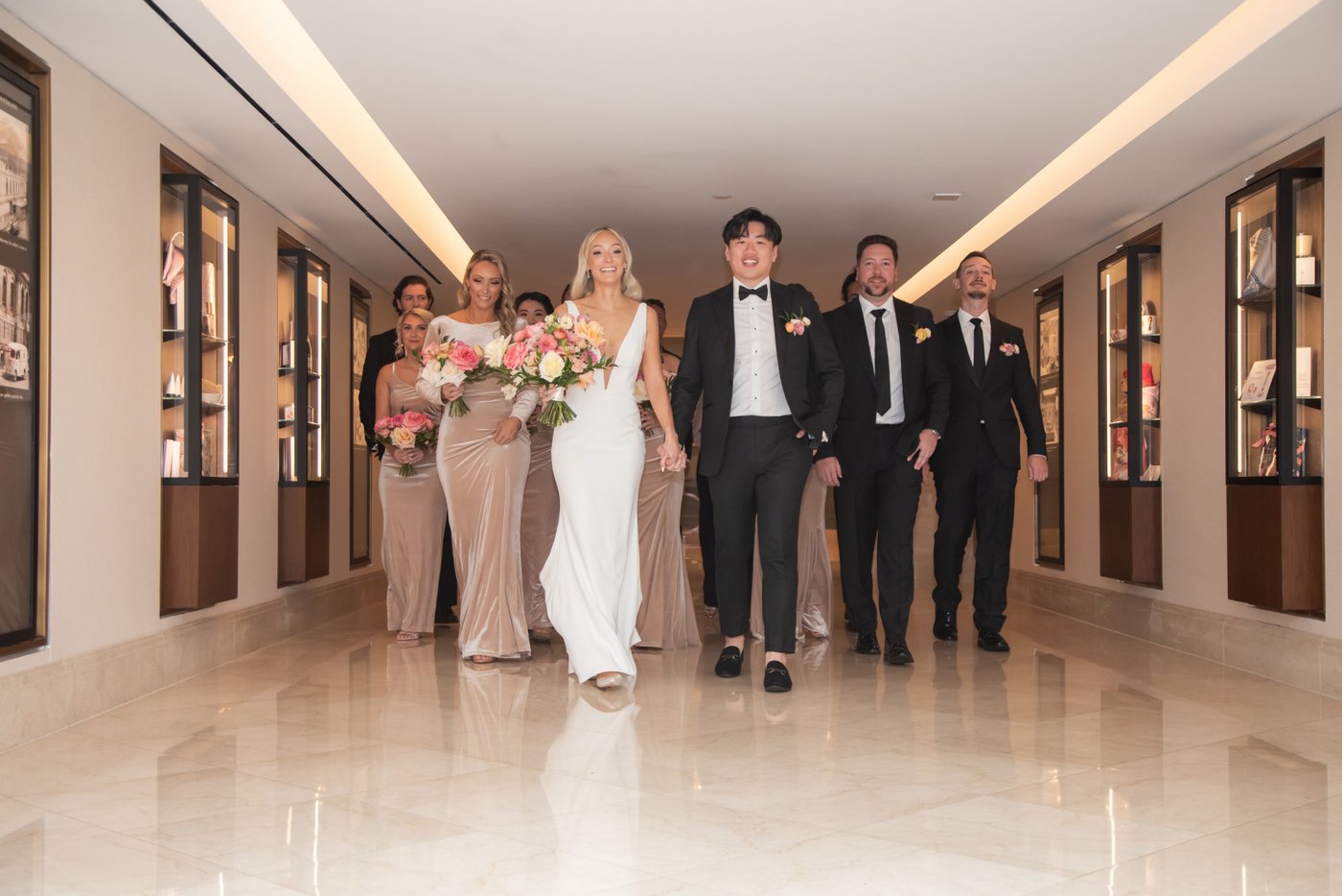 A creative, runway-style shot of the bride and groom leading the bridal party down the lobby hallway at the Langham Boston
