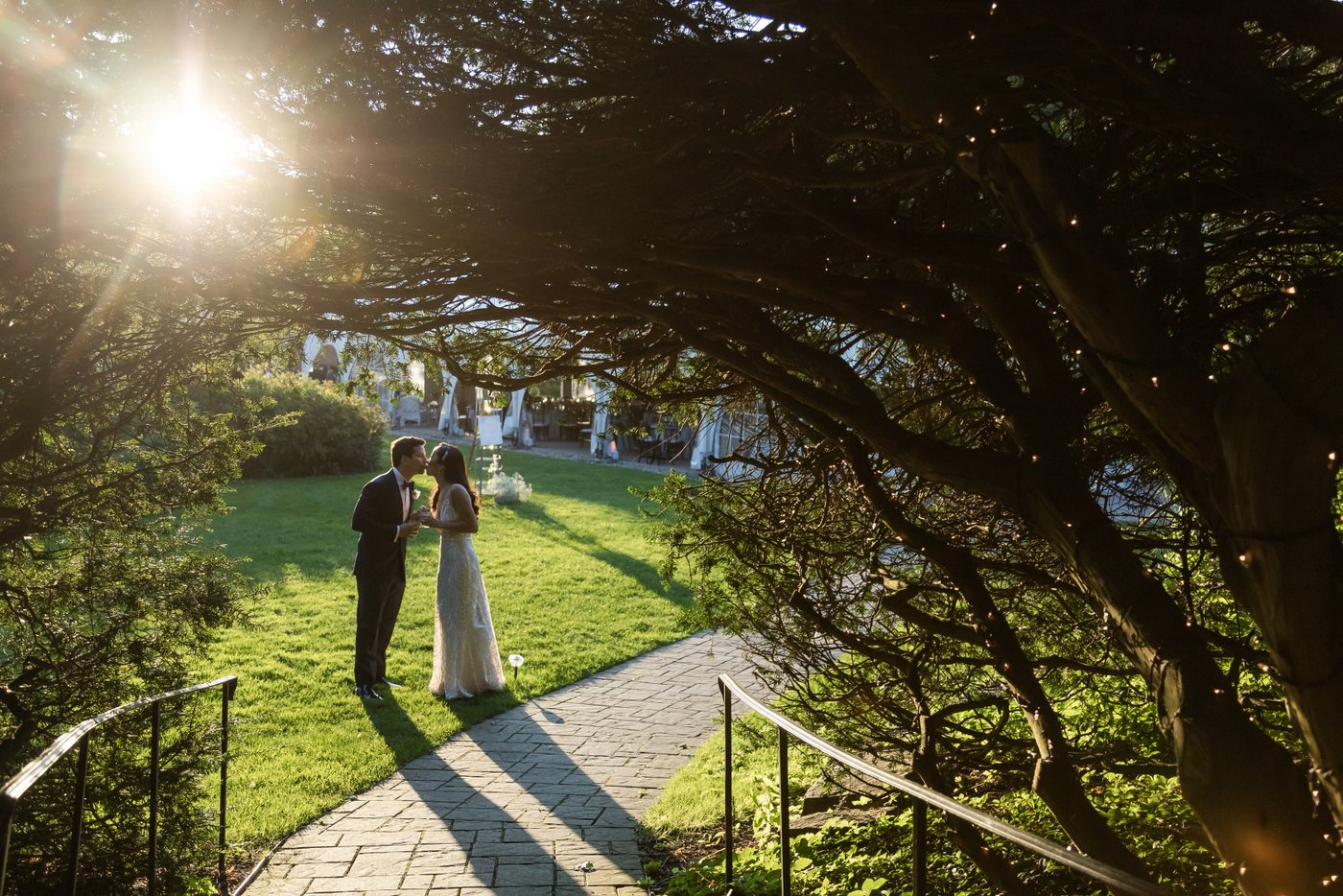 Framed by trees, with the setting sun casting a magical glow on the lawn, the bride and groom kiss near the wedding reception tent at Misselwood Estate.