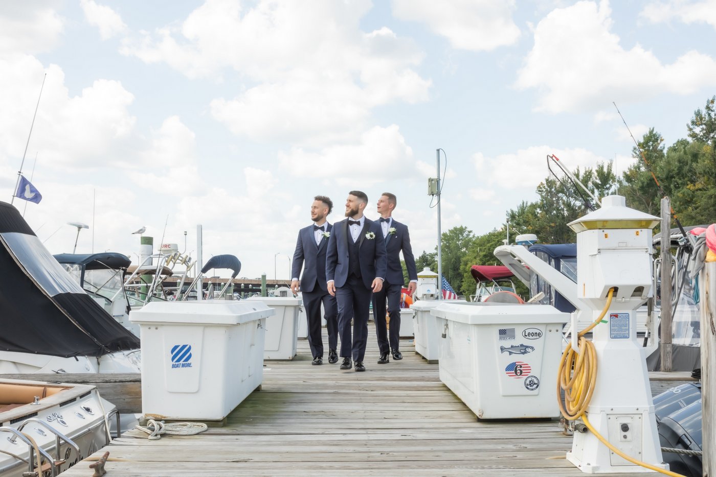 the groom and his groomsmen walking down the dock and looking into the distance