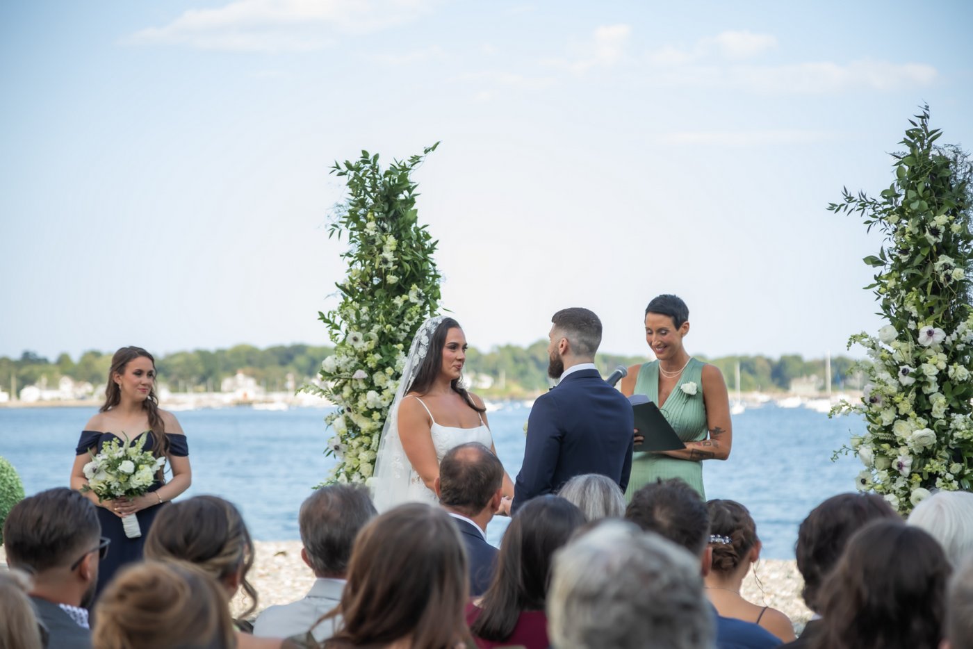 A photograph of the bride and groom at the altar shot at an angle with the blue ocean behind them on a beautiful summer day.