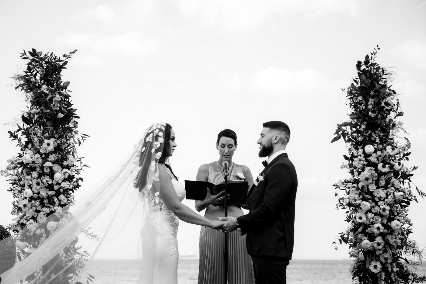 A black and white photograph of the bride and groom holding hands as the bride's veil floats behind her at an Oceanview of Nahant wedding photographed by Boston wedding photographers Spagnolo Photography.