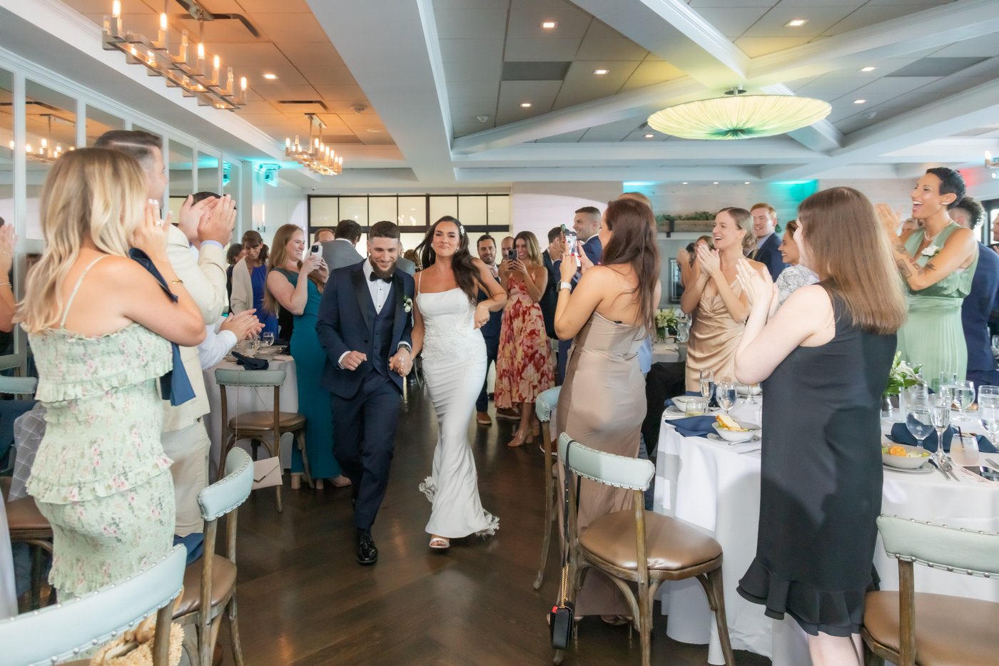 The bride and groom make their grand entrance into the reception hall as guests stand and clap at an Oceanview of Nahant wedding reception