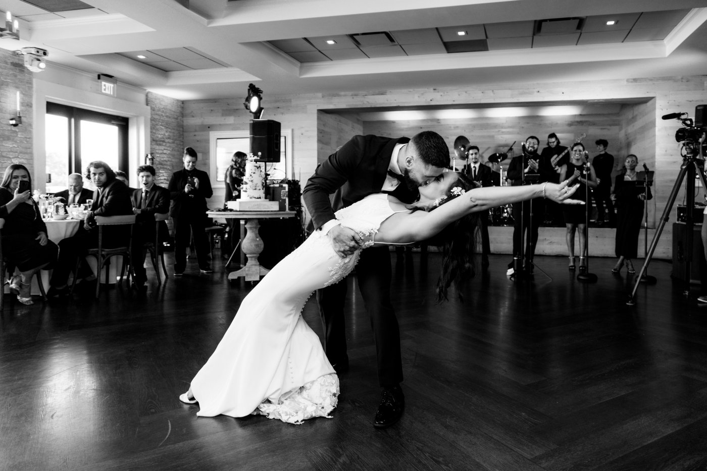 A black and white image of a groom dipping and kissing the bride during their romantic first dance at a lively wedding reception at Oceanview of Nahant on the North Shore of Massachusetts.
