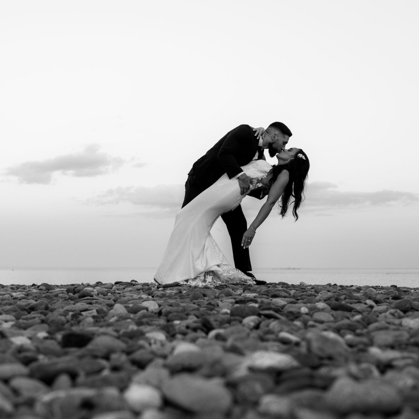 A black and white image of the groom dipping the bride on the beach at sunset during their Oceanview of Nahant wedding reception, square crop.