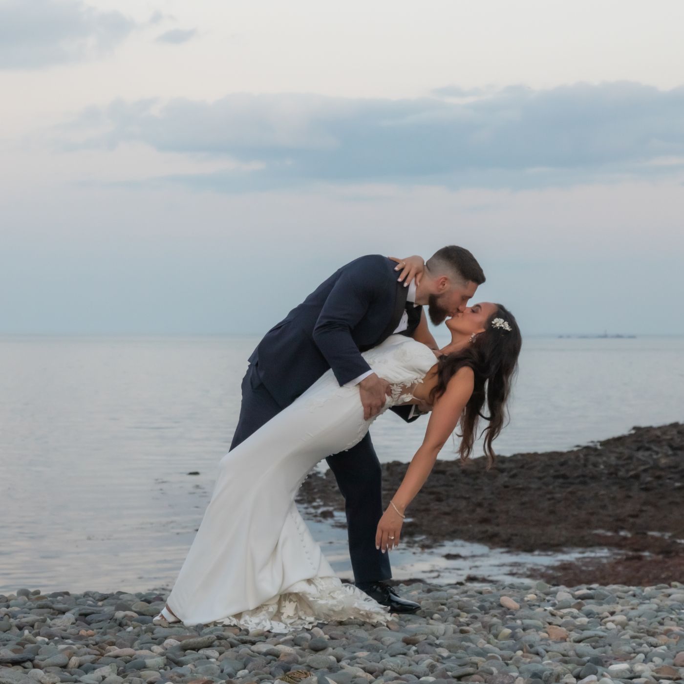 The groom dips the bride on the beach at sunset during their Oceanview of Nahant wedding reception.