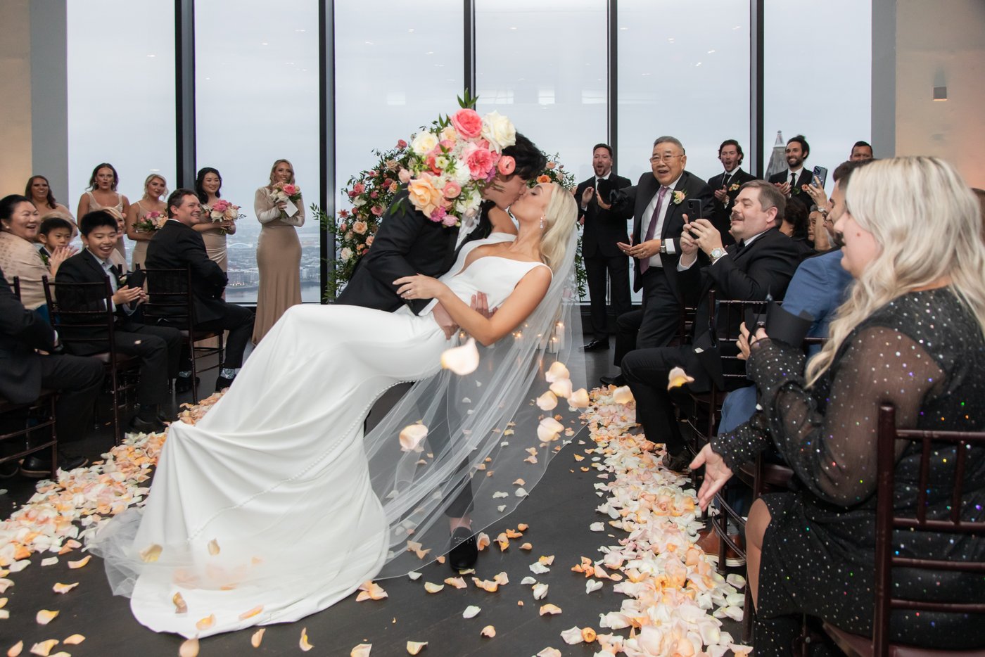 The groom dips the bride in the aisle as guests throw rose petals at the bride and groom at an elegant State Room Boston wedding.