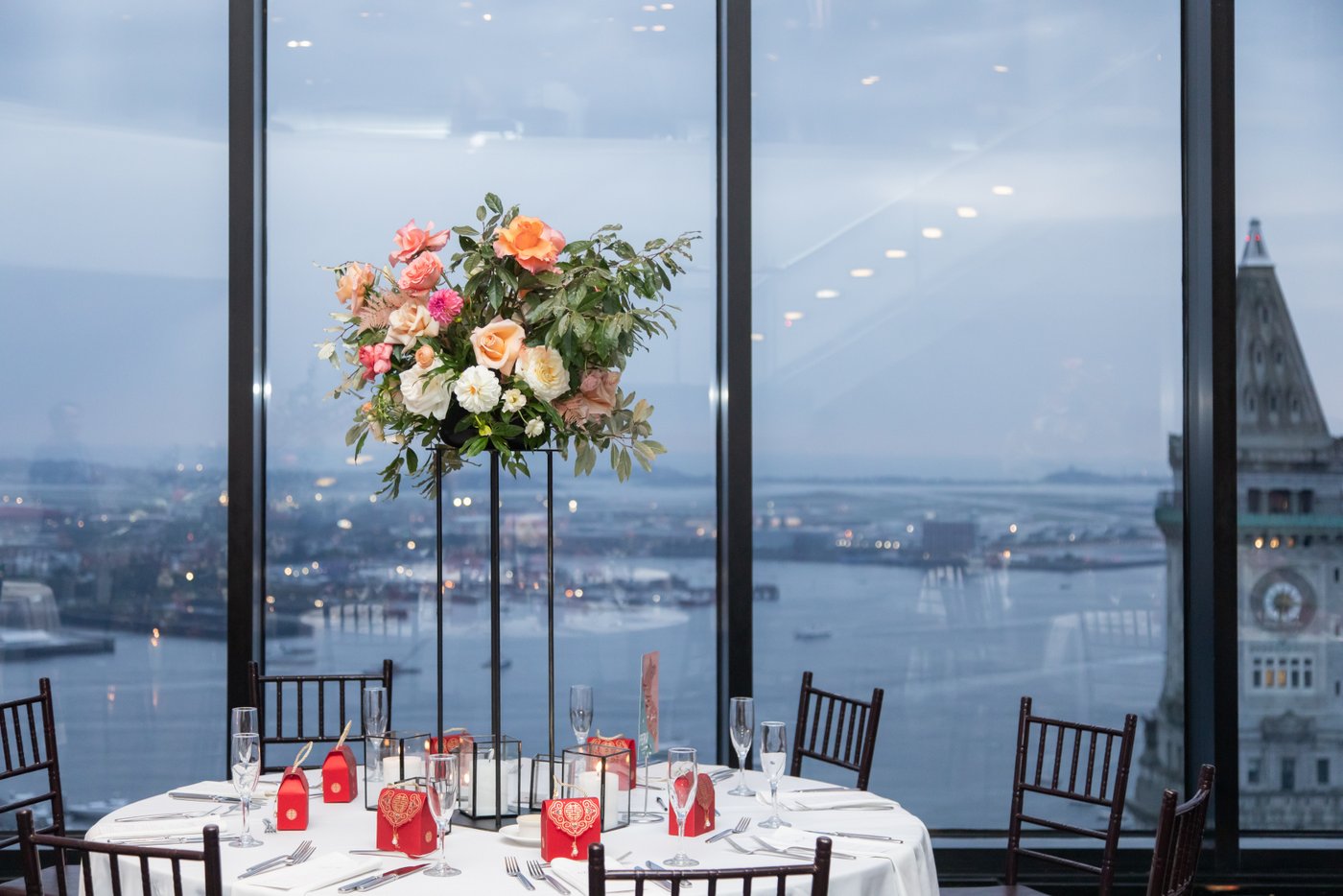 The table setting and a tall floral centerpiece at a State Room Boston wedding with the city skyline in the background.
