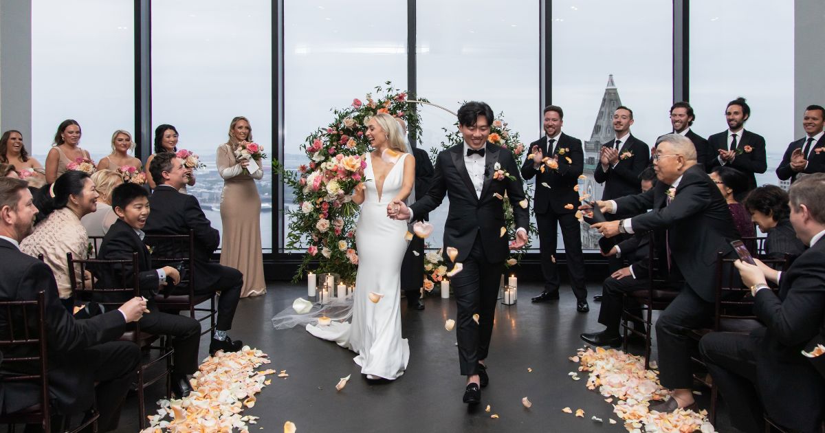 As the bride and groom begin walking down the aisle, guests throw rose petals at them at an elegant State Room wedding in Boston