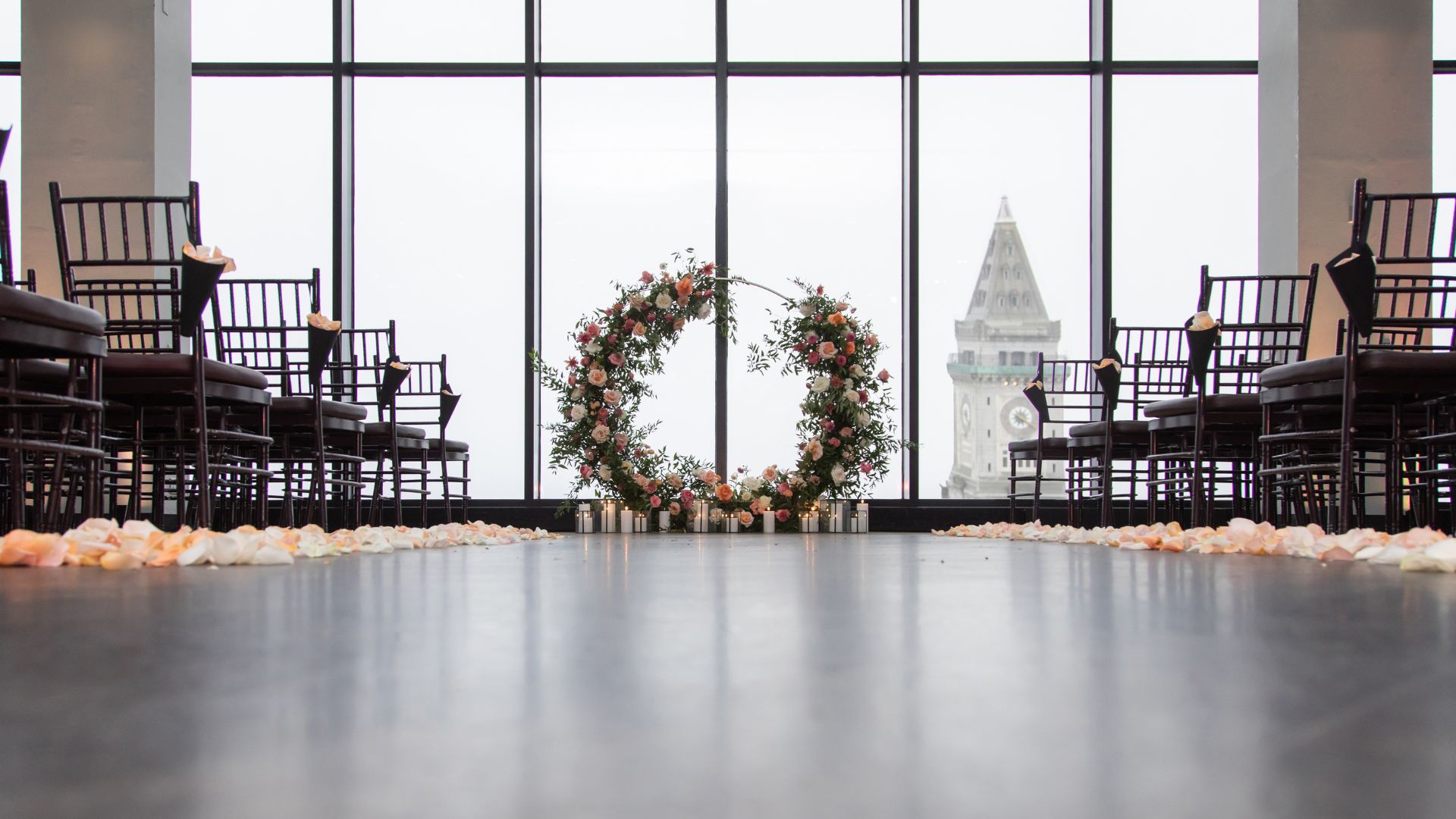 The State Room Boston wedding ceremony space setup before the wedding with a floral altar, candles, rose petals lining the aisle, and the Boston skyline behind the altar.