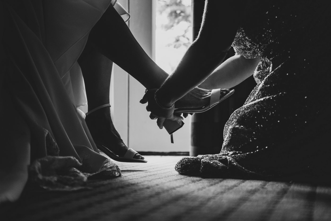 A black and white image of the mother of the bride helping the bride wear her shoes