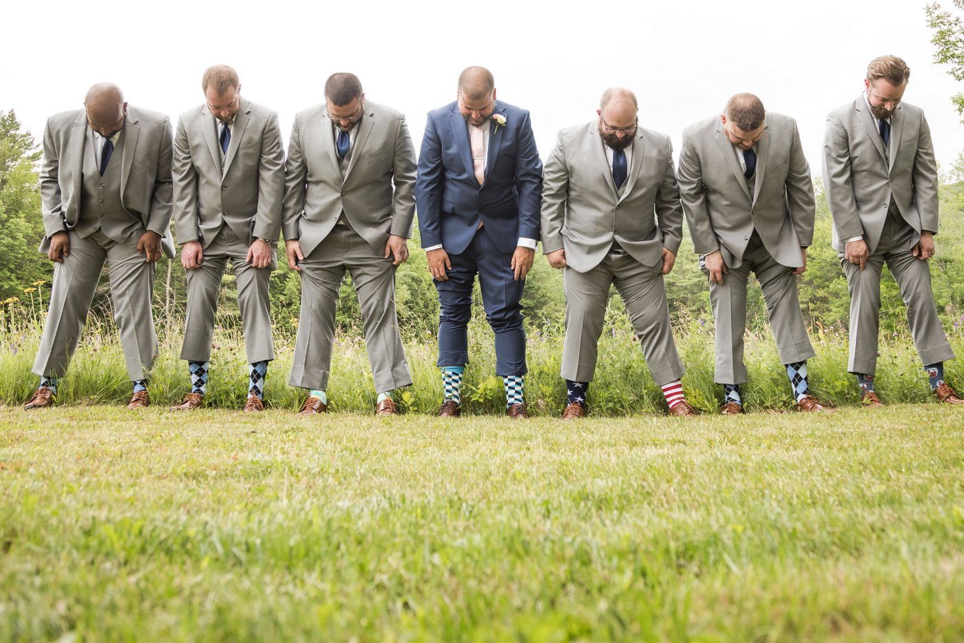 The groom and his groomsmen standing in a line and lifting up their pants to show off their colorful socks at a rustic barn wedding in Massachusetts, photographed by creative and candid Massachusetts wedding photographers Spagnolo Photography