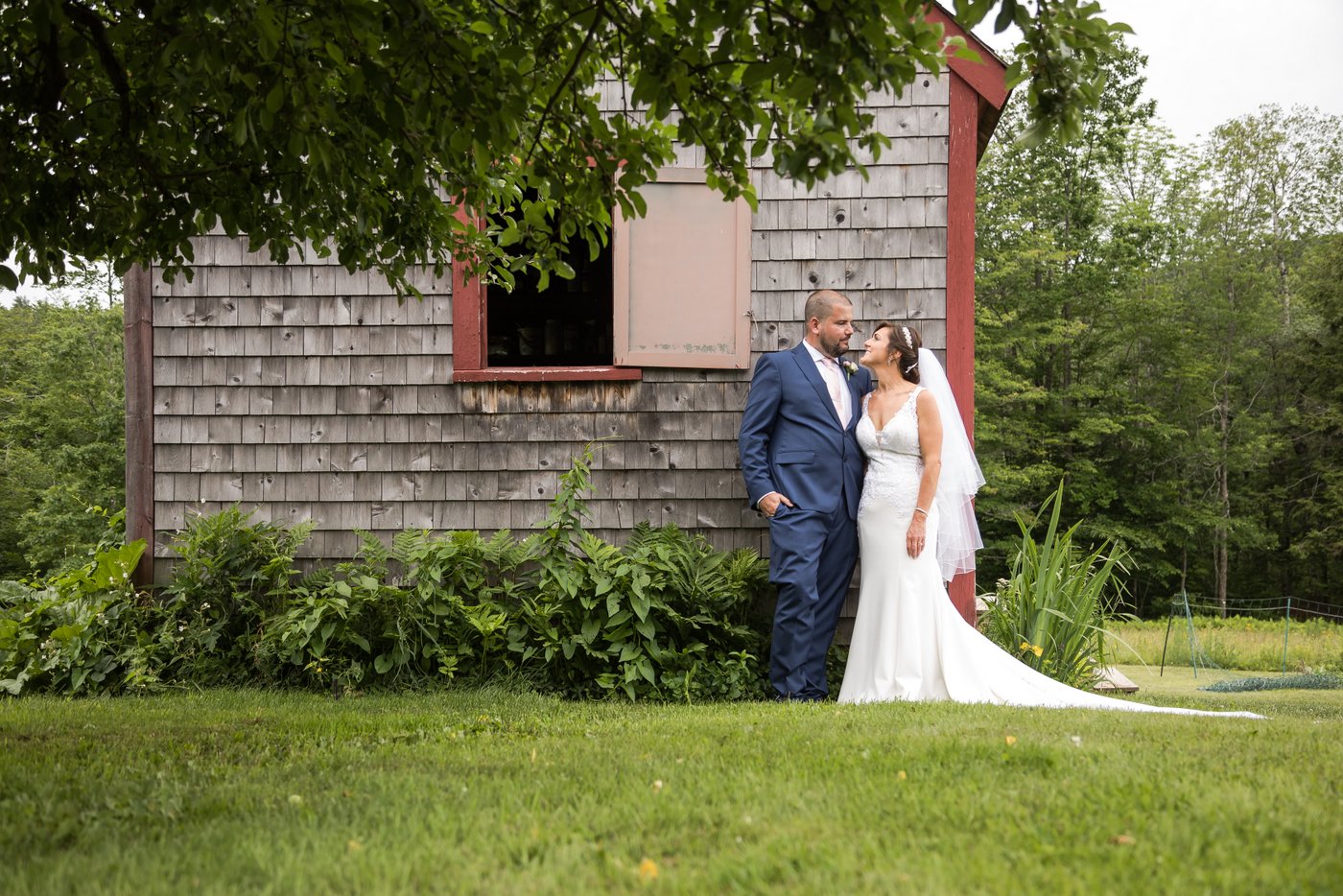 A bride and a groom look at each other while standing by a rustic cabin in Massachusetts