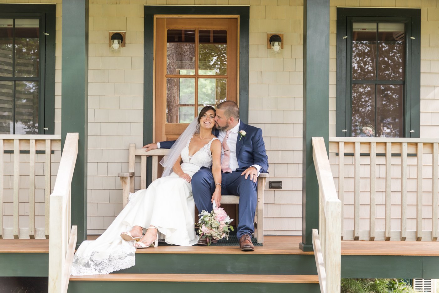 The bride and groom sit on a bench on the porch of a small cabin at a barn wedding in Massachusetts