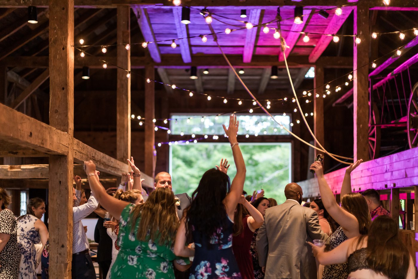 Guests dancing under string lights at a rustic wedding in a barn in Massachusetts
