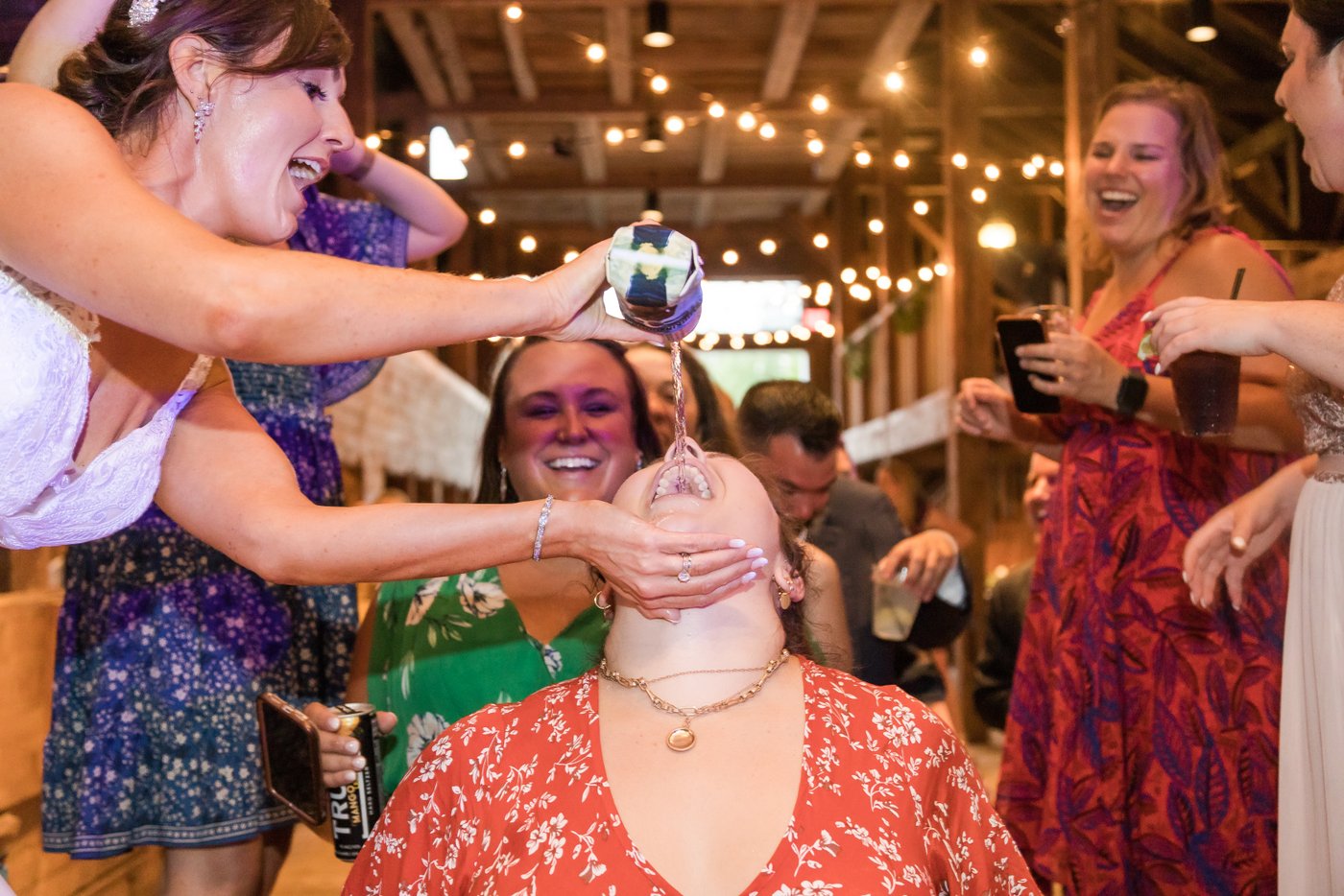 A bride pouring beer in the mouth of a guest at a barn wedding in Massachusetts