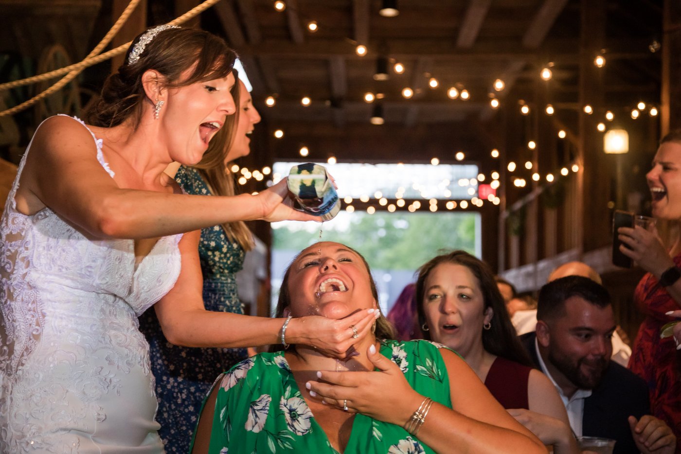 A bride pouring beer in the mouth of a guest at a barn wedding in Massachusetts